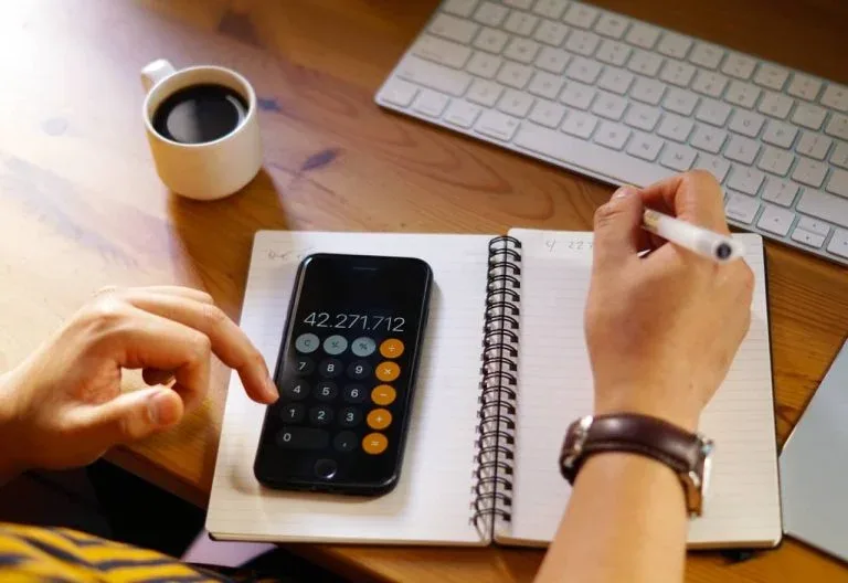 Mains tenant une calculatrice et un crayon devant un cahier.